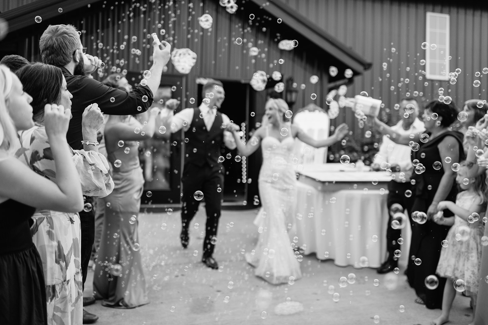 Bride and groom running through mock bubble exit as guests celebrate outside Rock Run Creek Barn.