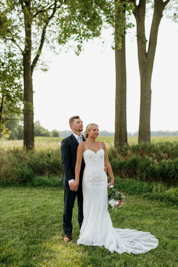 Bride and groom holding hands and standing in field at Rock Run Creek Barn in Goshen, Indiana.