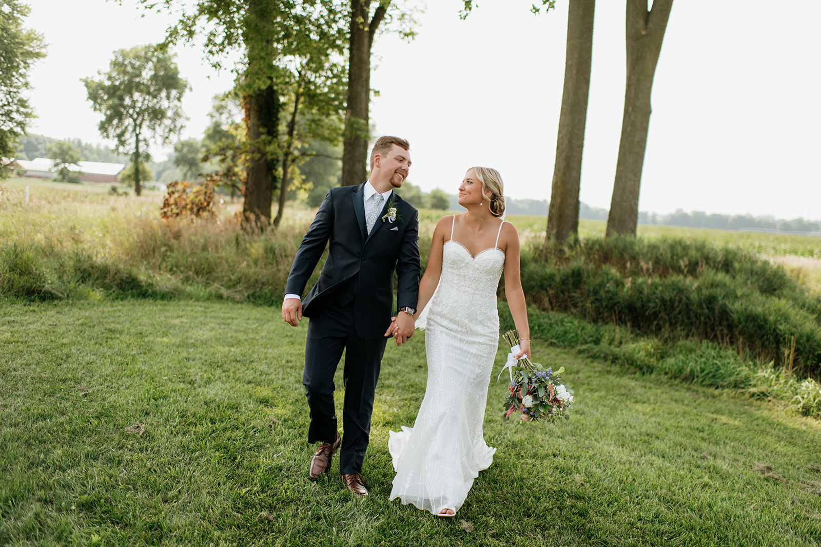 Couple walking hand-in-hand through the grass during golden hour at Rock Run Creek Barn wedding.