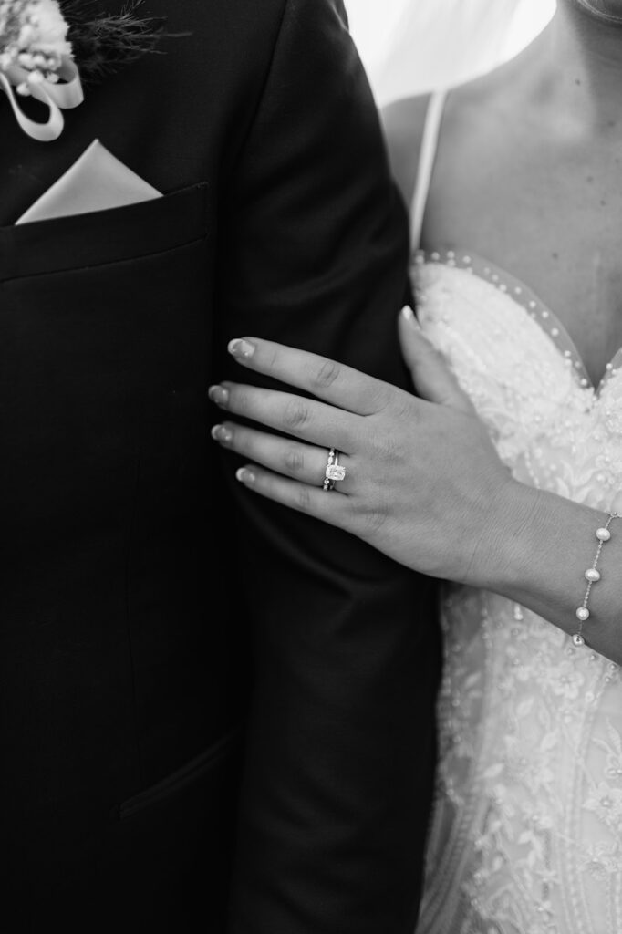 Black and white close up photo of a bride posing her hand on the grooms arm and showing off her ring