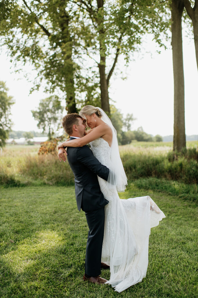 Groom lifting up the bride during golden hour portraits at Rock Run Creek Barn in Goshen, Indiana