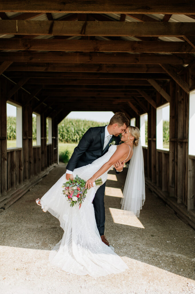 Groom dipping bride for a kiss inside the covered bridge at Rock Run Creek Barn.