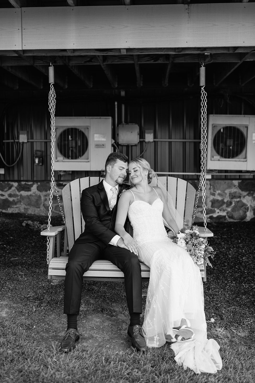 Couple sitting together on wooden porch swing outside the barn at Rock Run Creek Barn wedding.