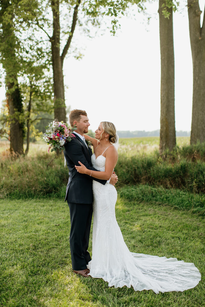Bride smiling up at groom while holding bouquet during sunset portraits at Rock Run Creek Barn.