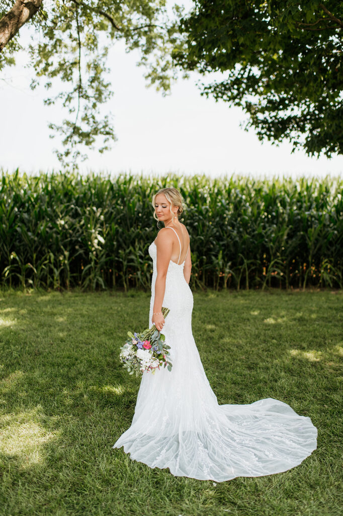 Bride standing in front of cornfield holding her bouquet at Rock Run Creek Barn in Goshen.