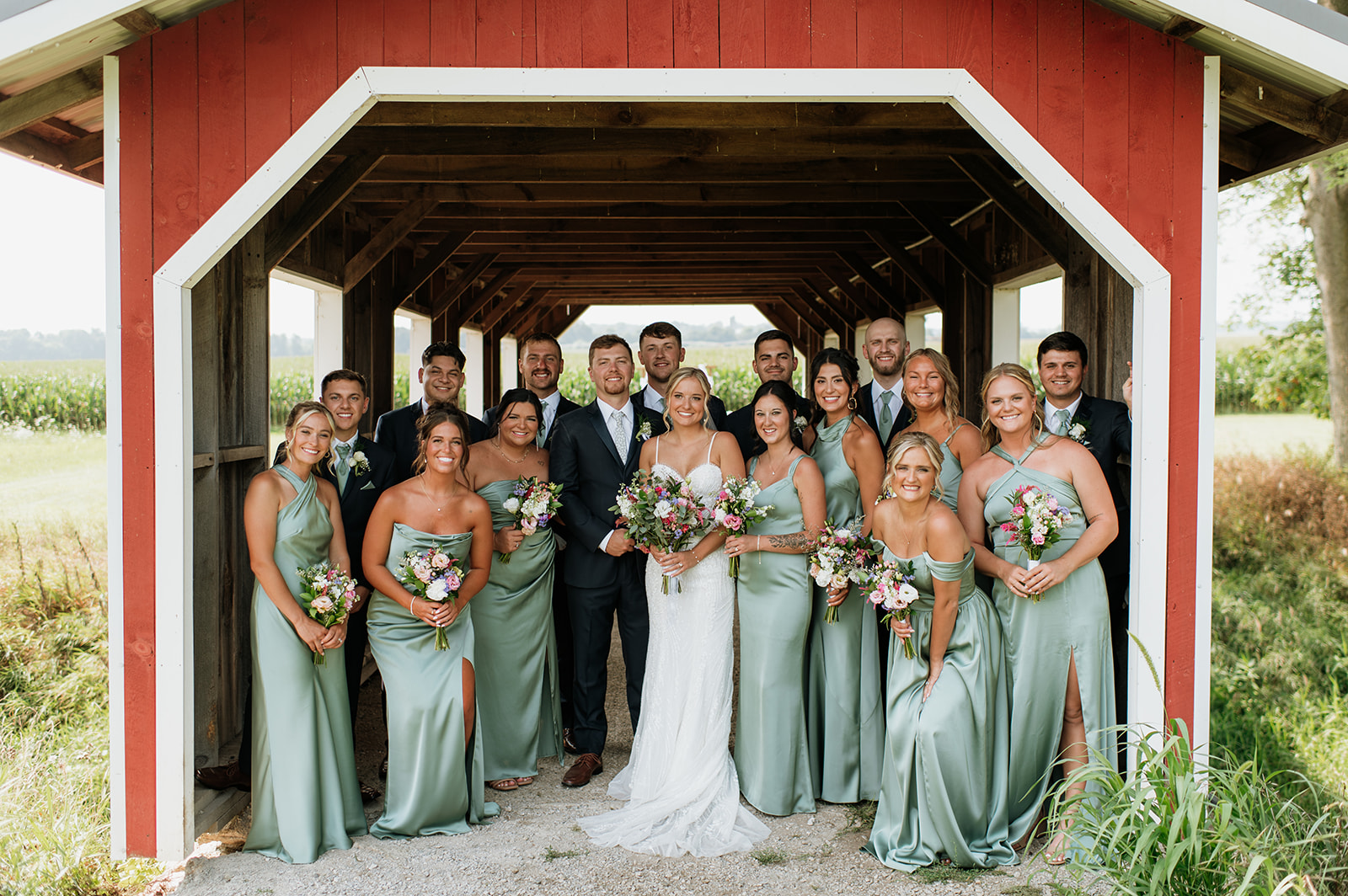 Bride and groom posing with their wedding party underneath the covered bridge at Rock Run Creek Barn wedding venue
