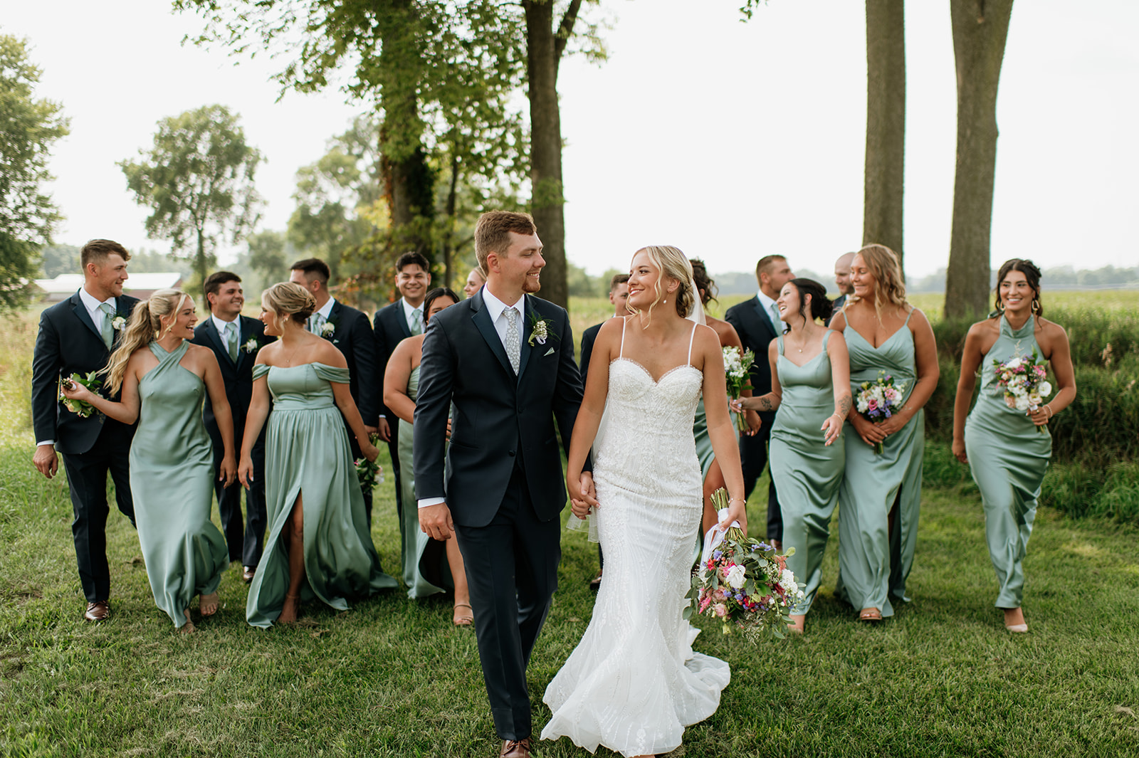 Bride and groom walking hand in hand with their wedding party during their Rock Run Creek Barn wedding in Goshen, Indiana