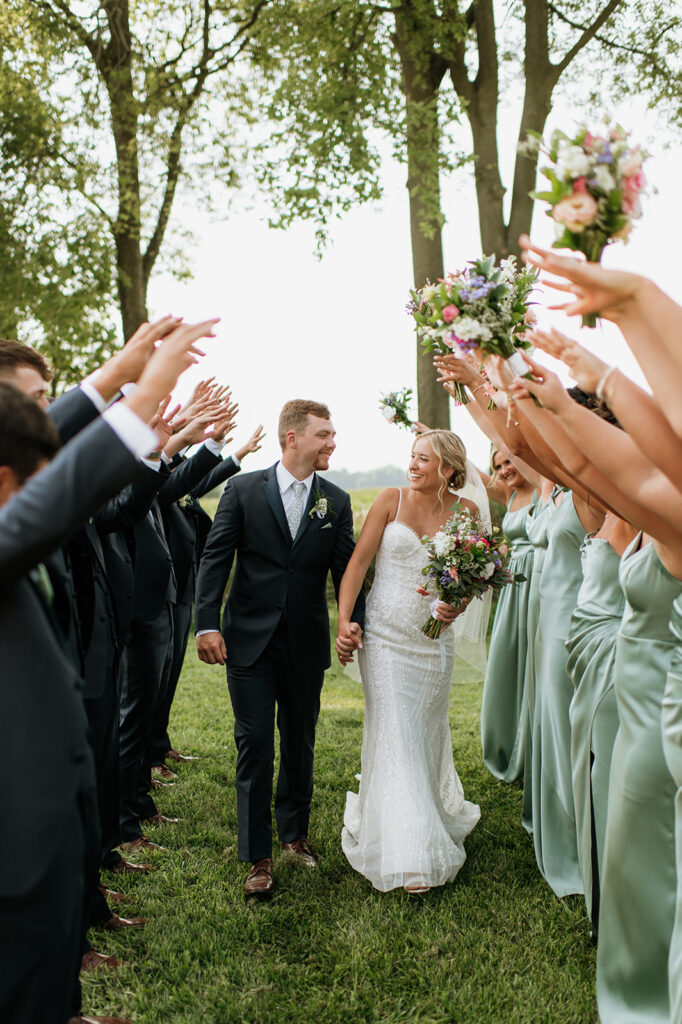 Bride and groom walking hand in hand with their wedding party during their Rock Run Creek Barn wedding in Goshen, Indiana