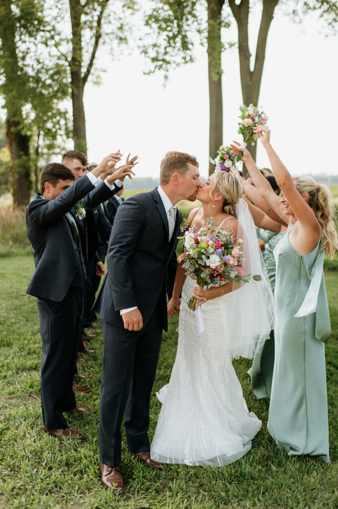 Bride and groom kissing while surrounded by their wedding party during their Rock Run Creek Barn wedding in Goshen, Indiana