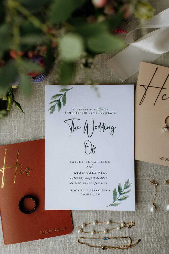 Wedding detail shot of invites, jewelry, his and her vow books, and bouquet 