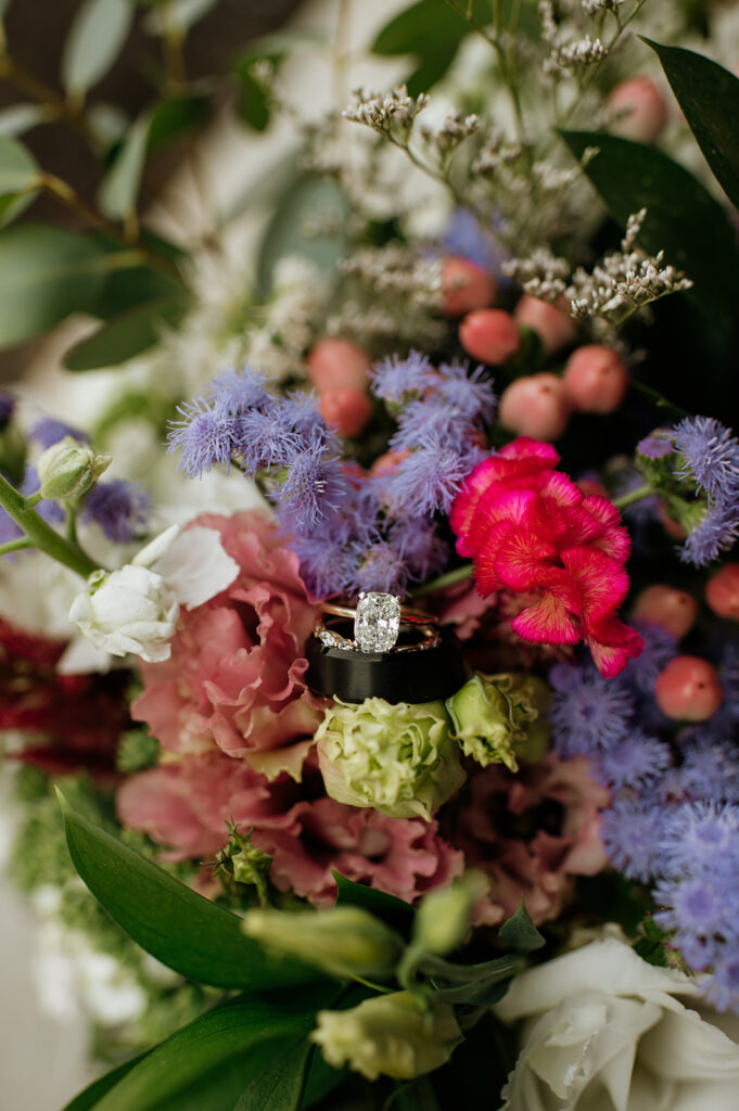 Close up detail shot of the brides rings and grooms wedding band in the brides colorful wedding bouquet 