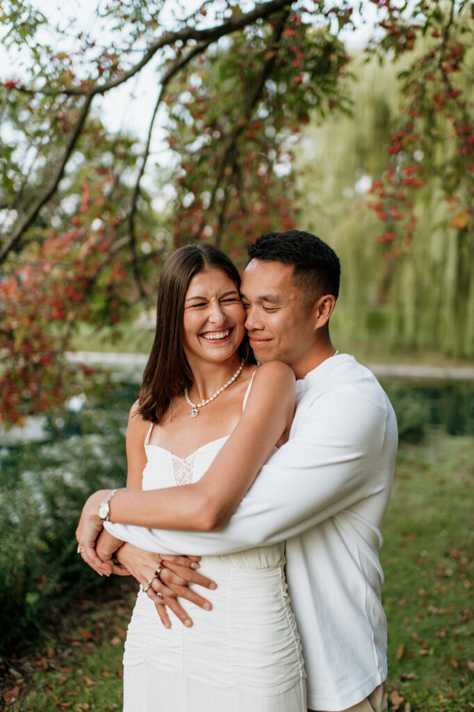 Couple hugging near Lake Marian surrounded by colorful trees during their Saint Mary’s College engagement photos.
