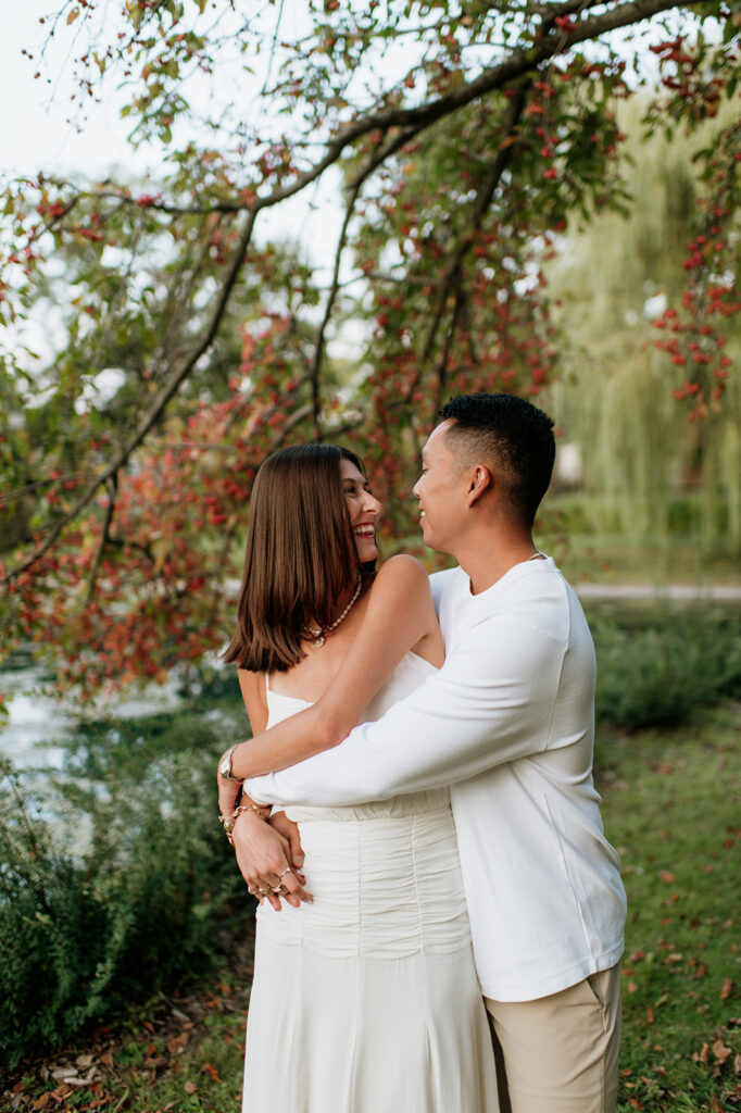 Couple smiling near Lake Marian surrounded by colorful trees during their Saint Mary’s College engagement photos.