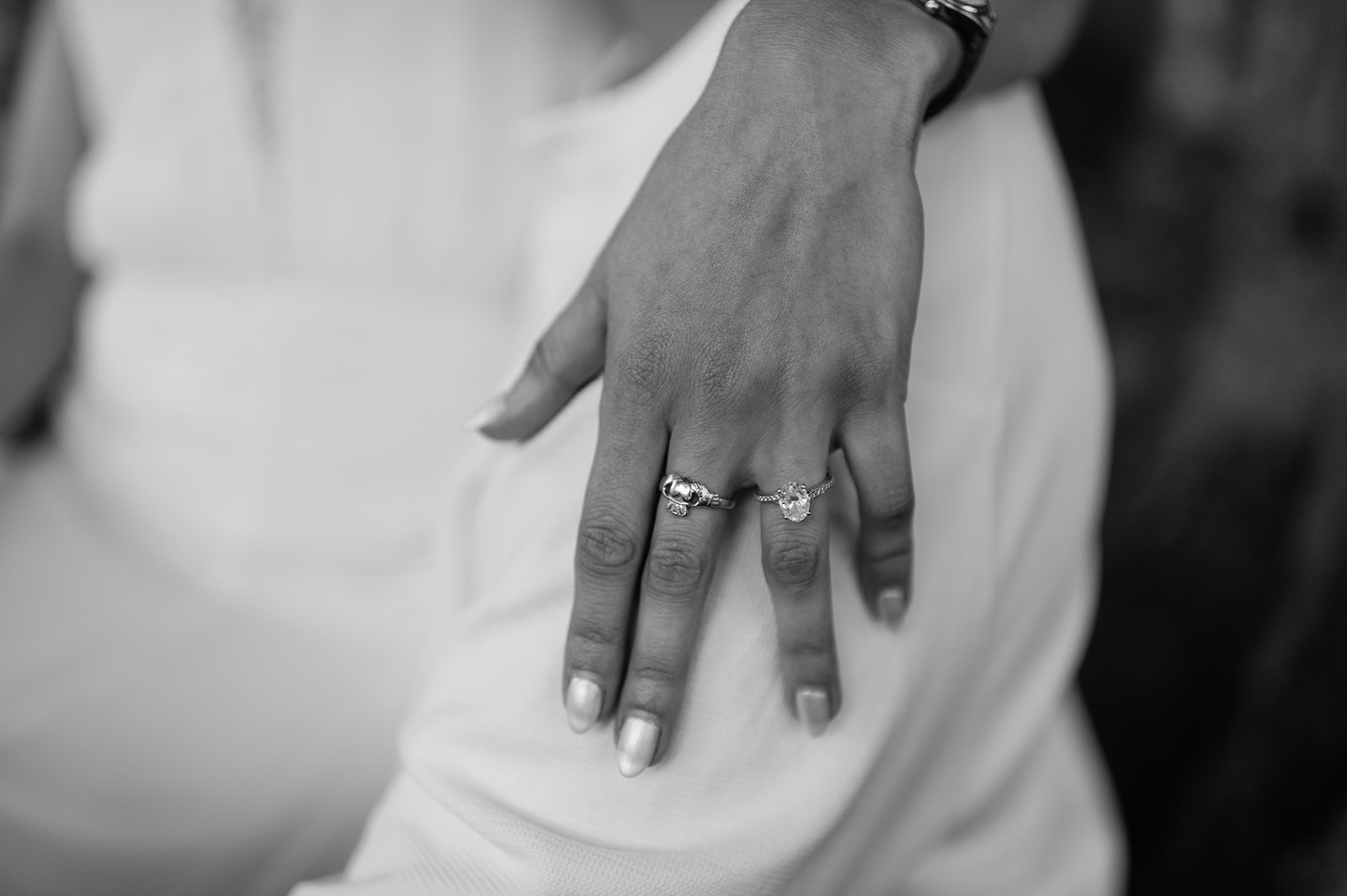 Black and white close-up of engagement ring and jewelry on her hand resting gently on his arm.
