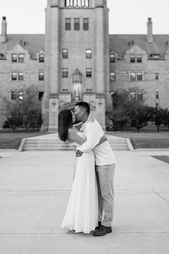 Black and white image of couple sharing a kiss in front of the steps of LeMans Hall at Saint Mary’s College.