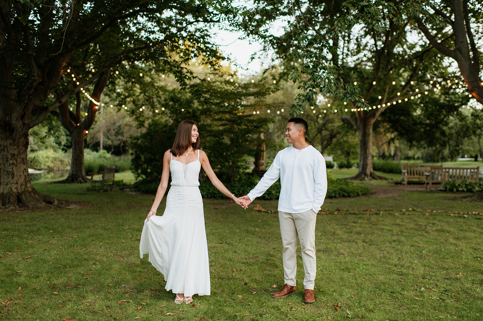 Couple smiling and holding hands beneath trees wrapped in string lights at Saint Mary’s College.