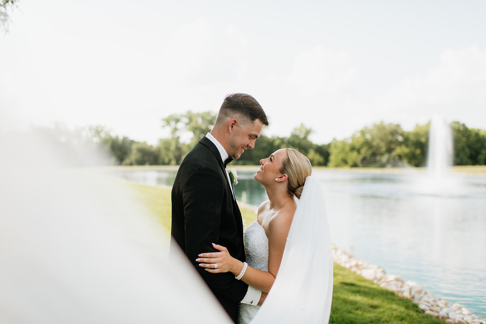 Wide shot of the bride and groom posing by the water during their summer Clubhouse Venue wedding portraits in Indiana