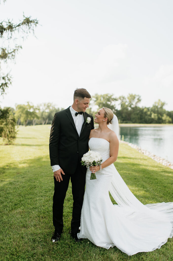 Bride and groom smiling at each other while standing near the water at The Clubhouse venue.