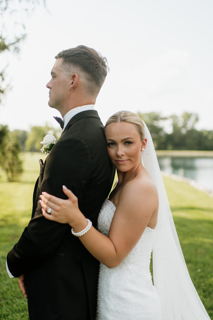 Bride hugging groom from behind and looking at the camera during portraits on the grounds.