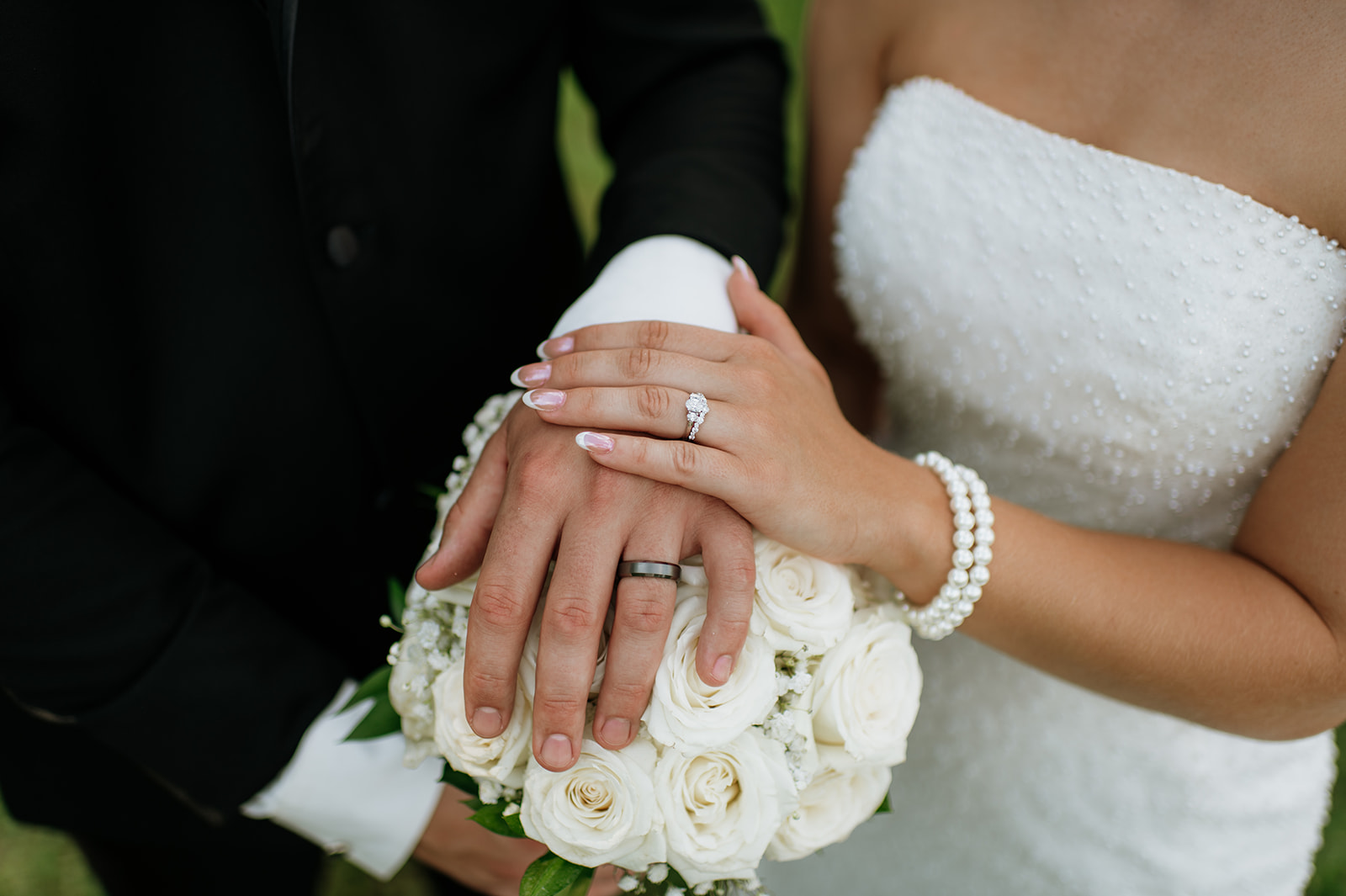 Close up shot of a bride and groom resting their hand on the brides classic white bouquet showcasing their wedding rings.