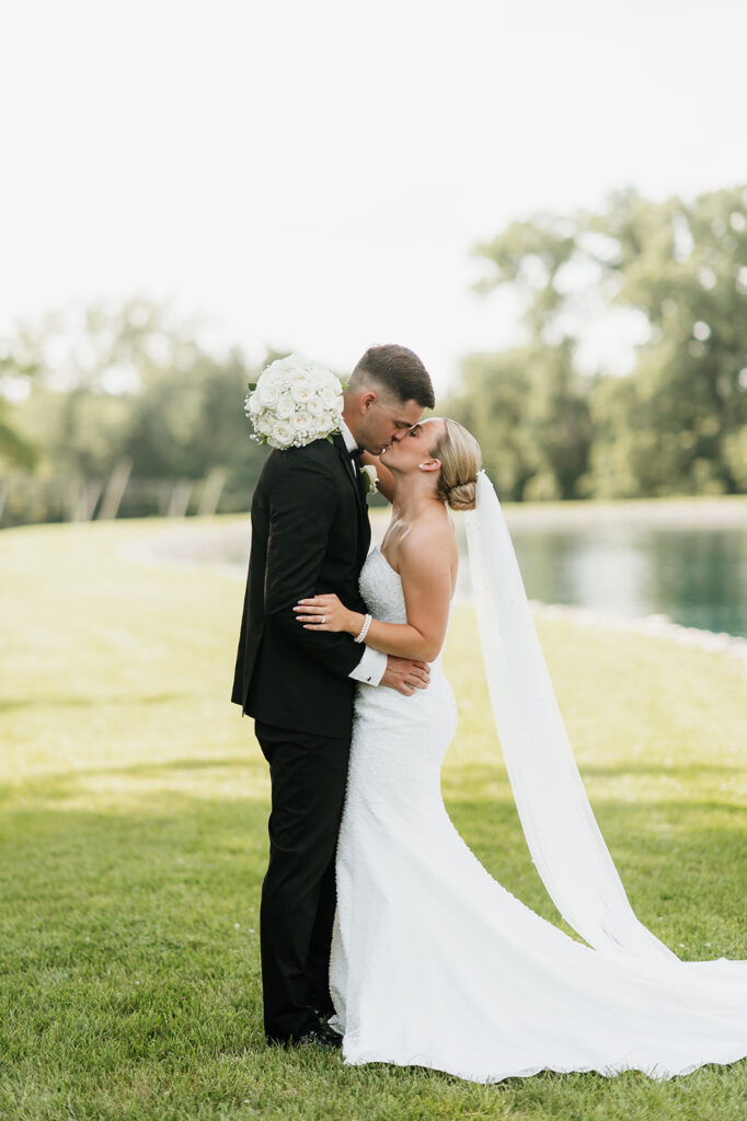 Bride and groom kissing close together by the pond at The Clubhouse venue during newlywed portraits.