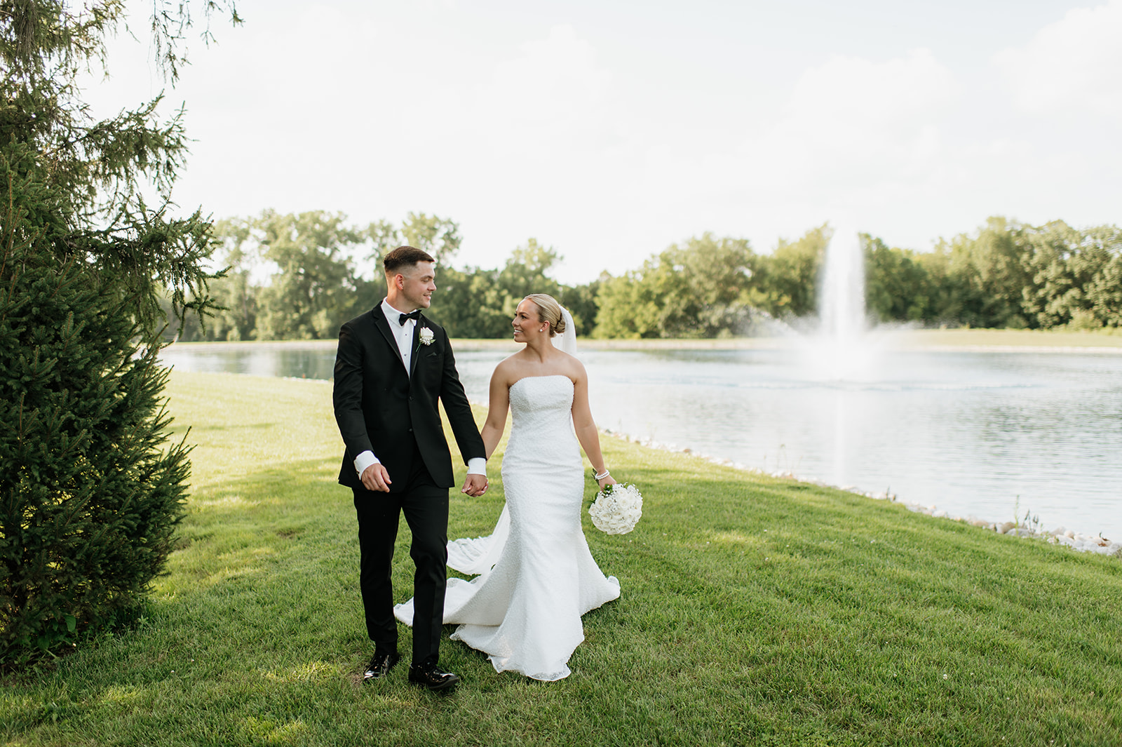 Bride and groom walking hand in hand beside the pond at The Clubhouse venue during summer portraits.