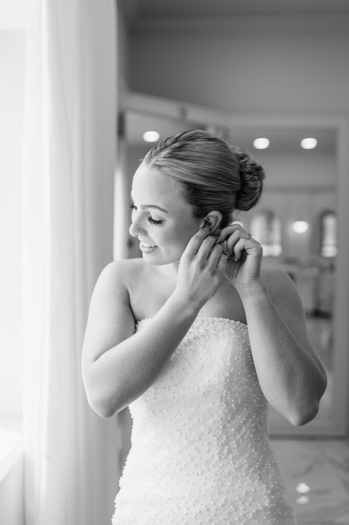 Bride putting on earrings by the window in the bridal suite at The Clubhouse Venue.