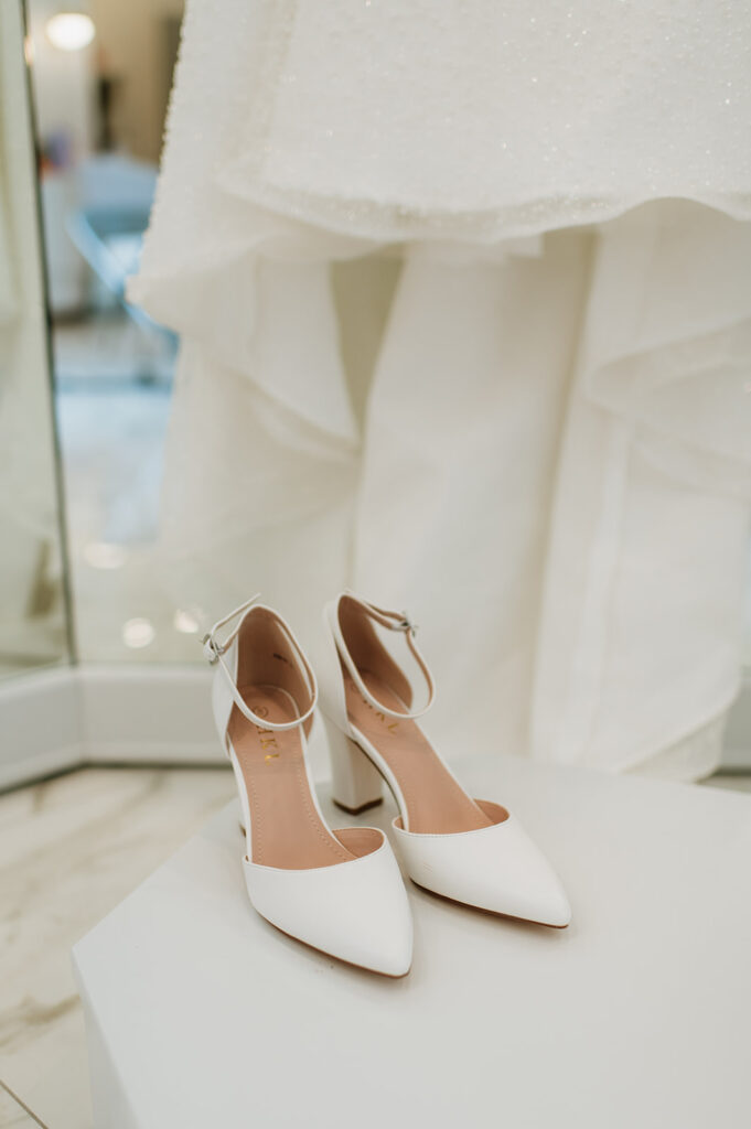 Close up wedding detail shot of the brides shoes next to her hanging wedding dress