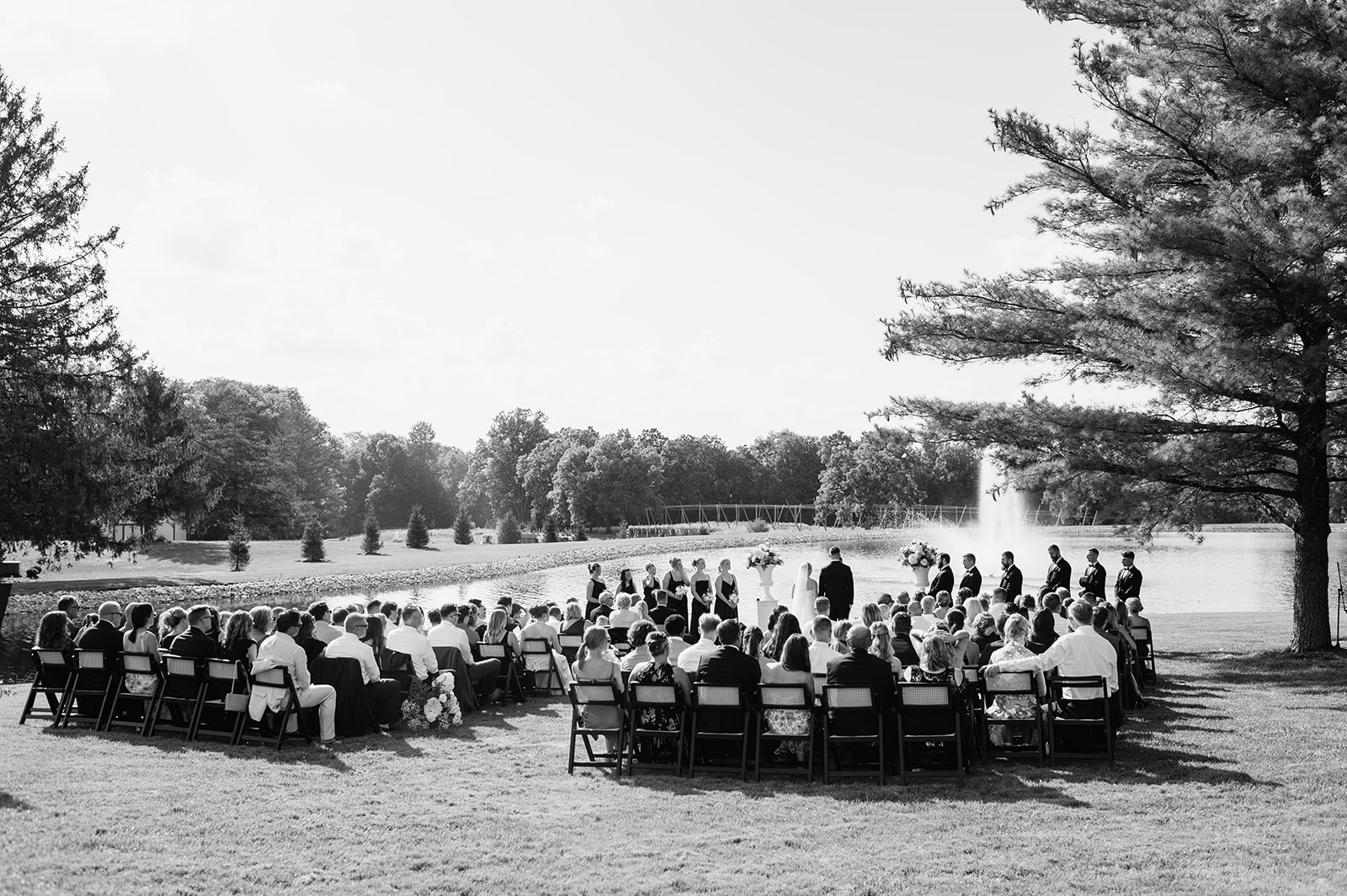 Wide ceremony view with guests seated by the pond and fountain at The Clubhouse Venue.