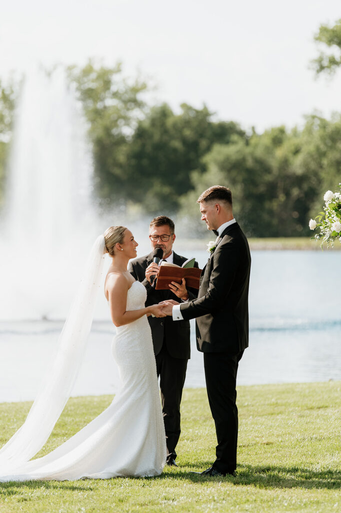 Bride and groom standing at the altar with the pond and fountain behind them at The Clubhouse Venue.