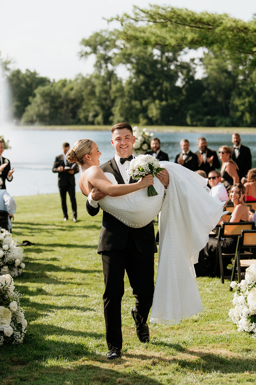 Groom carrying the bride down the aisle after the ceremony on the grounds of The Clubhouse Venue.