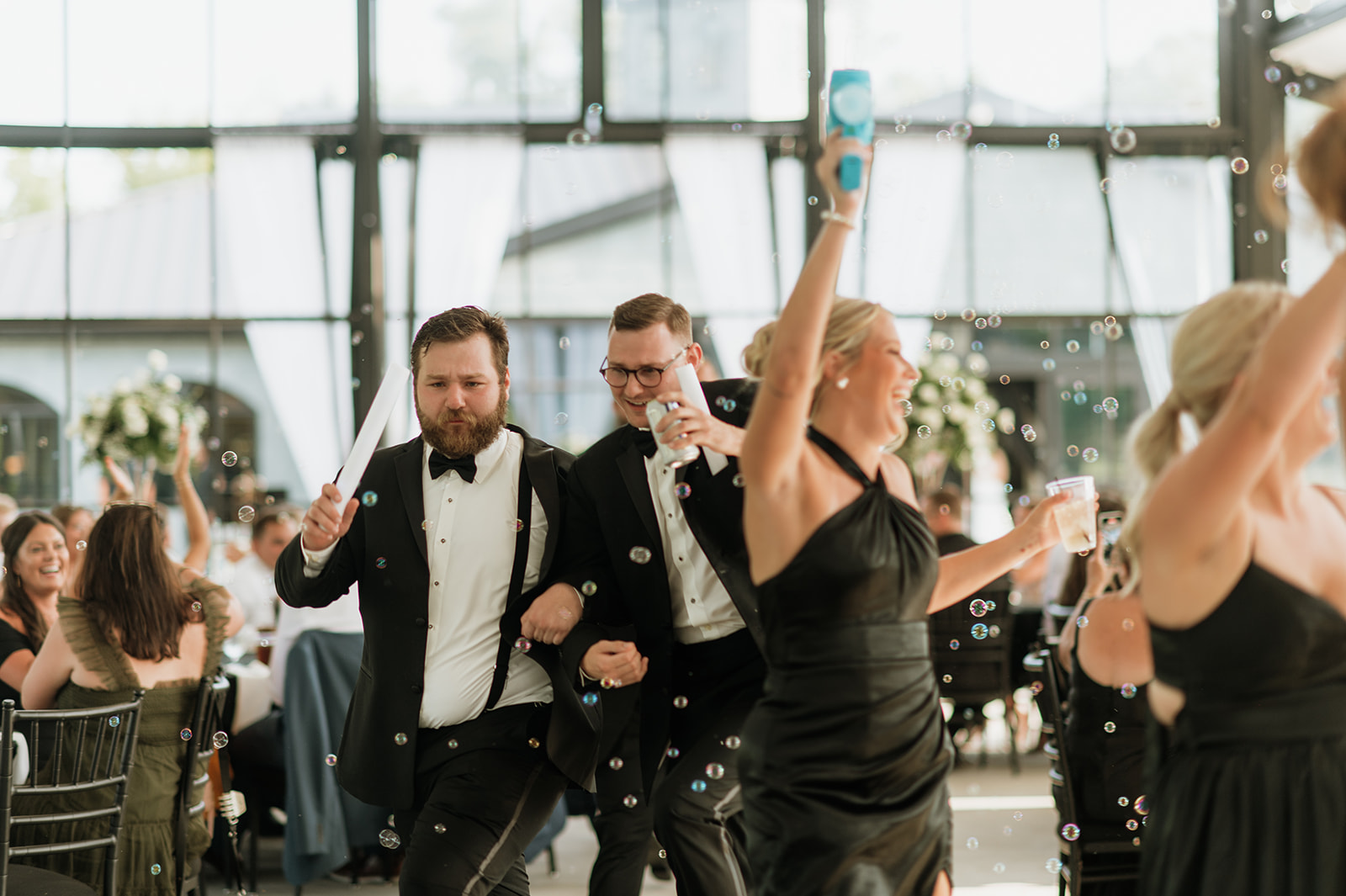 Wedding party entering The Clubhouse Venue reception with bubble guns and smiles.