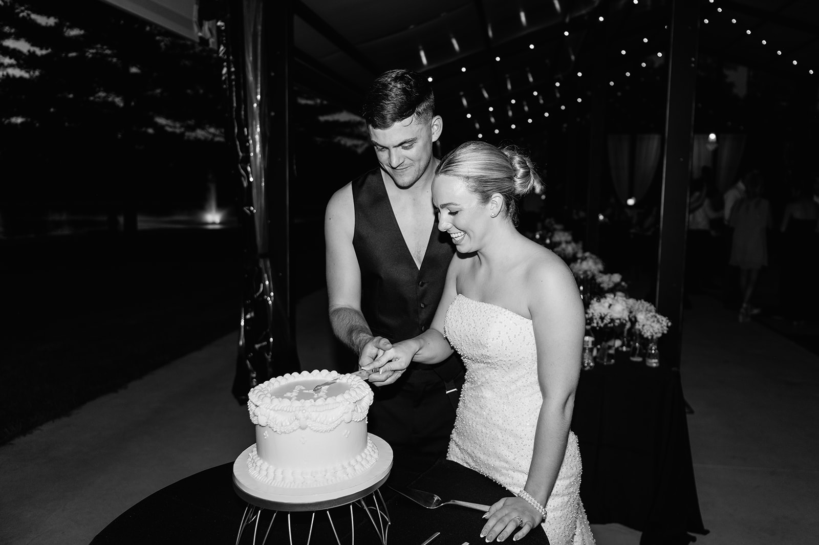 Black and white photo of a bride and groom cutting their wedding cake at The Clubhouse Venue.
