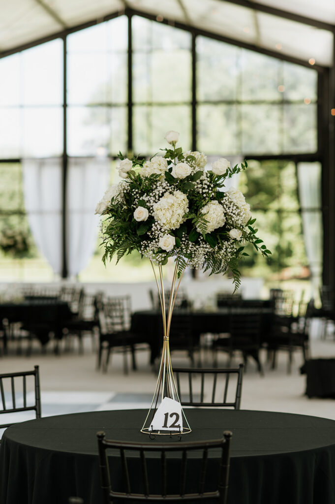 Tall white floral centerpiece on a black linen table inside The Clubhouse Venue reception space.