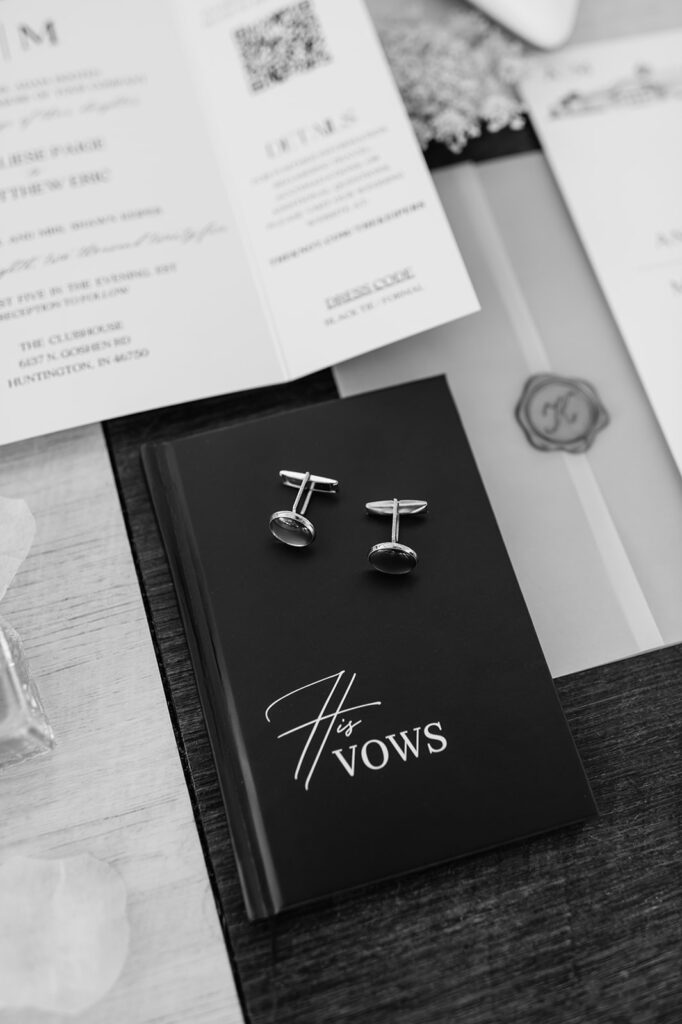Black and white photo of grooms wedding details with cufflinks and his vow book