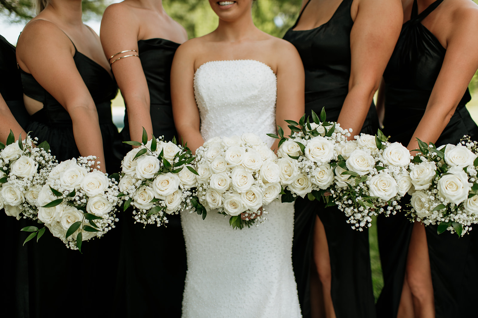 Close-up of white rose bouquets held by the bride and bridesmaids in black dresses at The Clubhouse Venue.