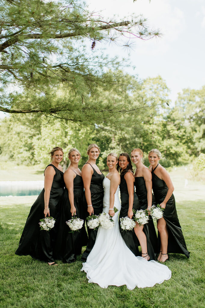 Bridesmaids lined up with the bride, holding white bouquets on the lawn at The Clubhouse Venue.