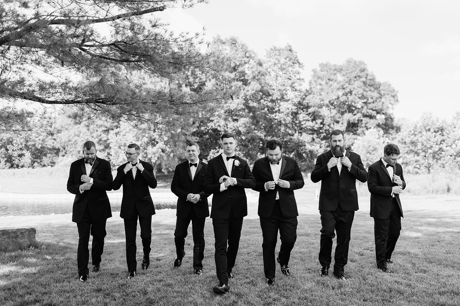 Black and white photo of the groom and his groomsmen walking towards the camera on the lawn at The Clubhouse Venue.