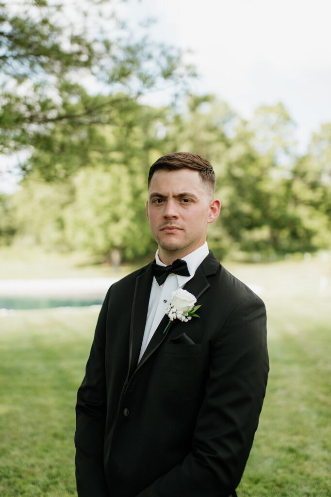 Close up of a groom standing for a portrait in front of the pond at The Clubhouse Venue.