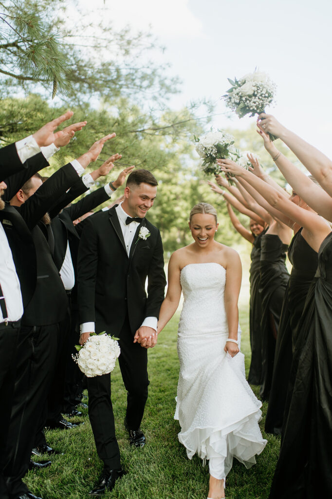 Bride and groom walking through a tunnel of raised bouquets and hands from their wedding party at The Clubhouse Venue.