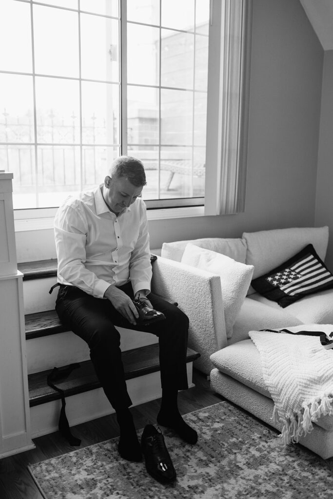 Black and white photo of a groom putting his shoes on as he gets ready for his Chicago wedding day.