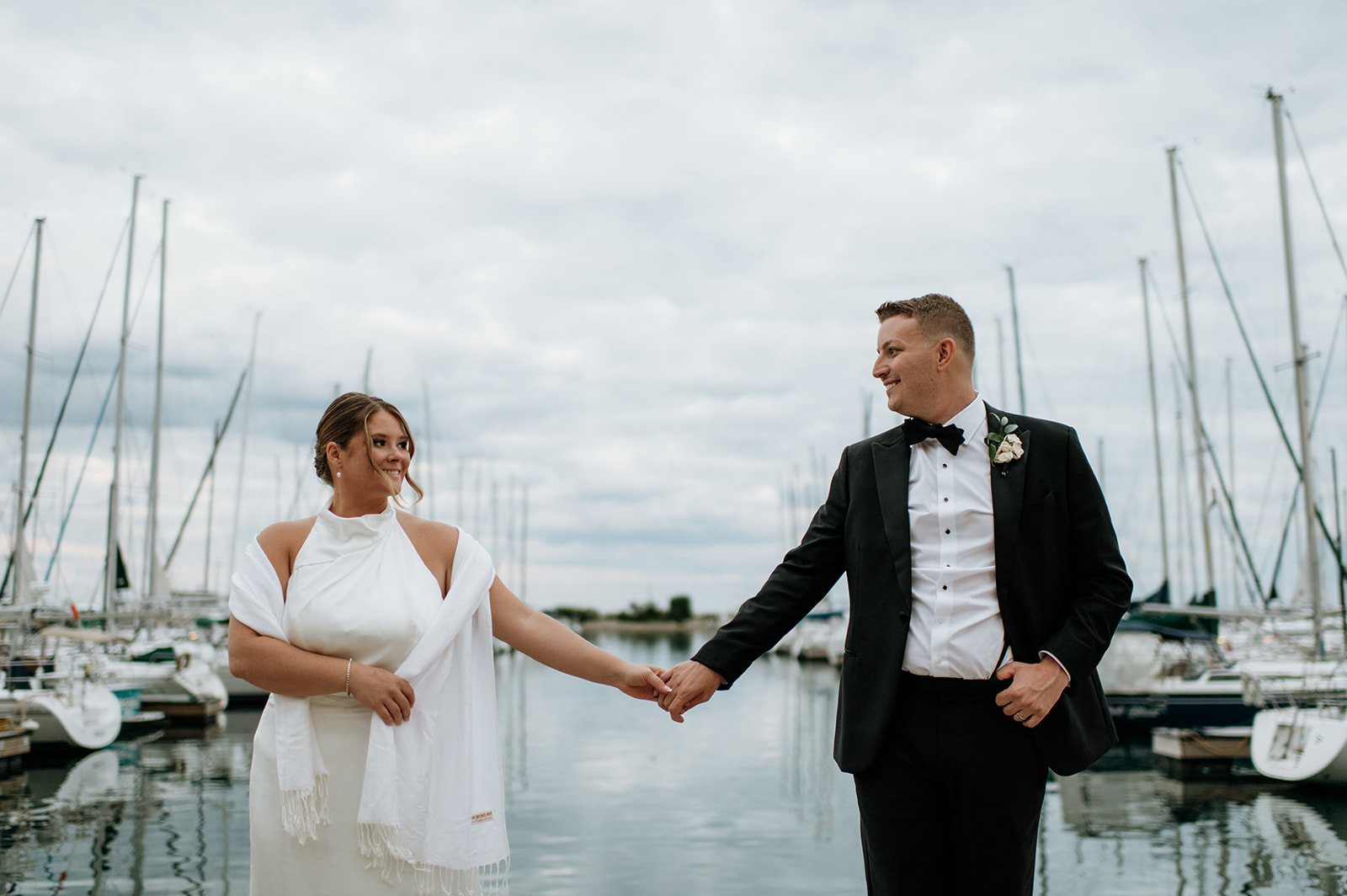 Bride and groom smiling at each other during evening portraits at the marina before boarding the yacht.