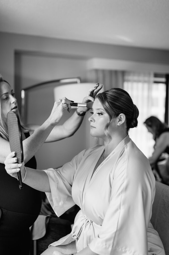 Bride getting her makeup done as she holds up a mirror to look at herself.
