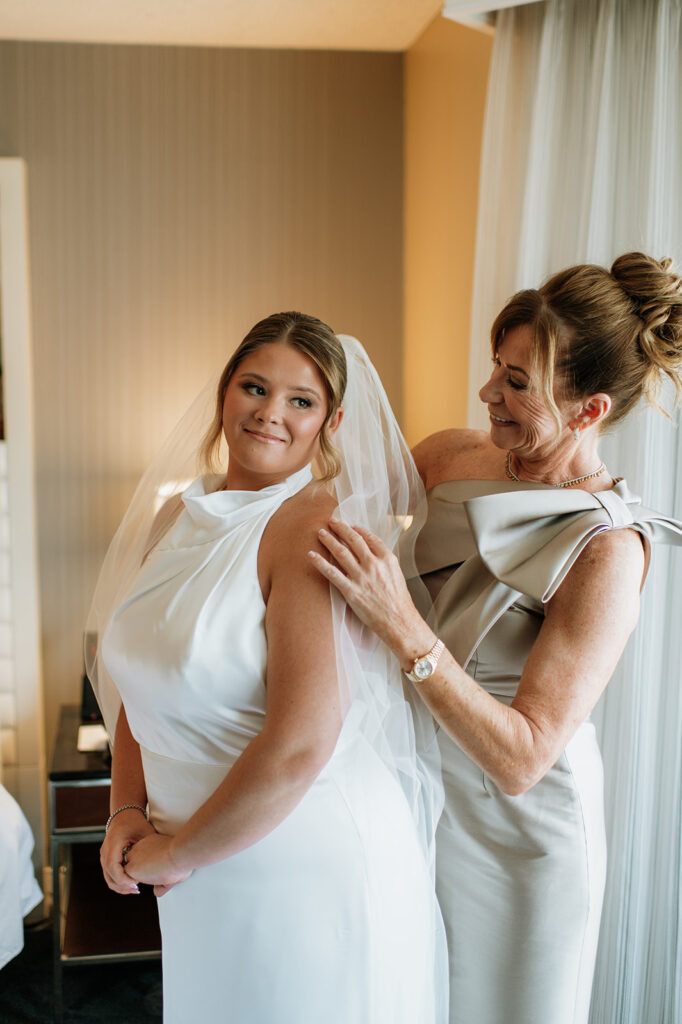 Mother helping the bride adjust her veil in a hotel room.