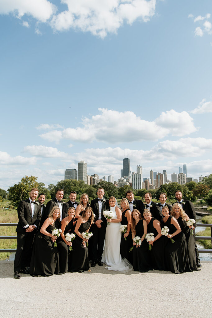 Full wedding party posing with the Chicago skyline visible in the background.