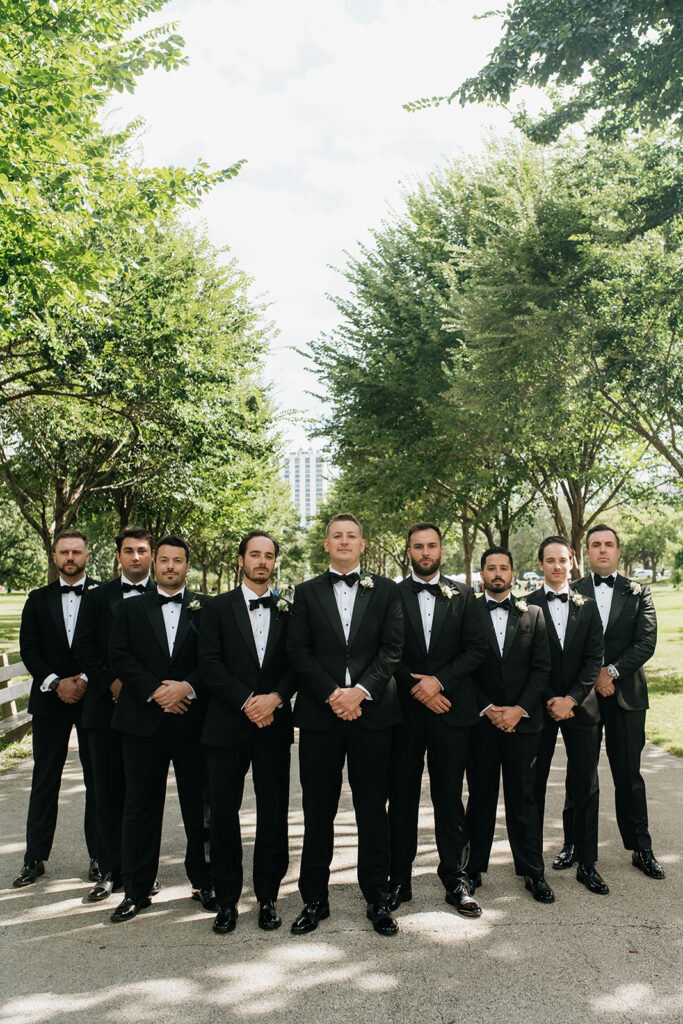 Groomsmen posing together in black tuxedos along a tree-lined path in Lincoln Park.