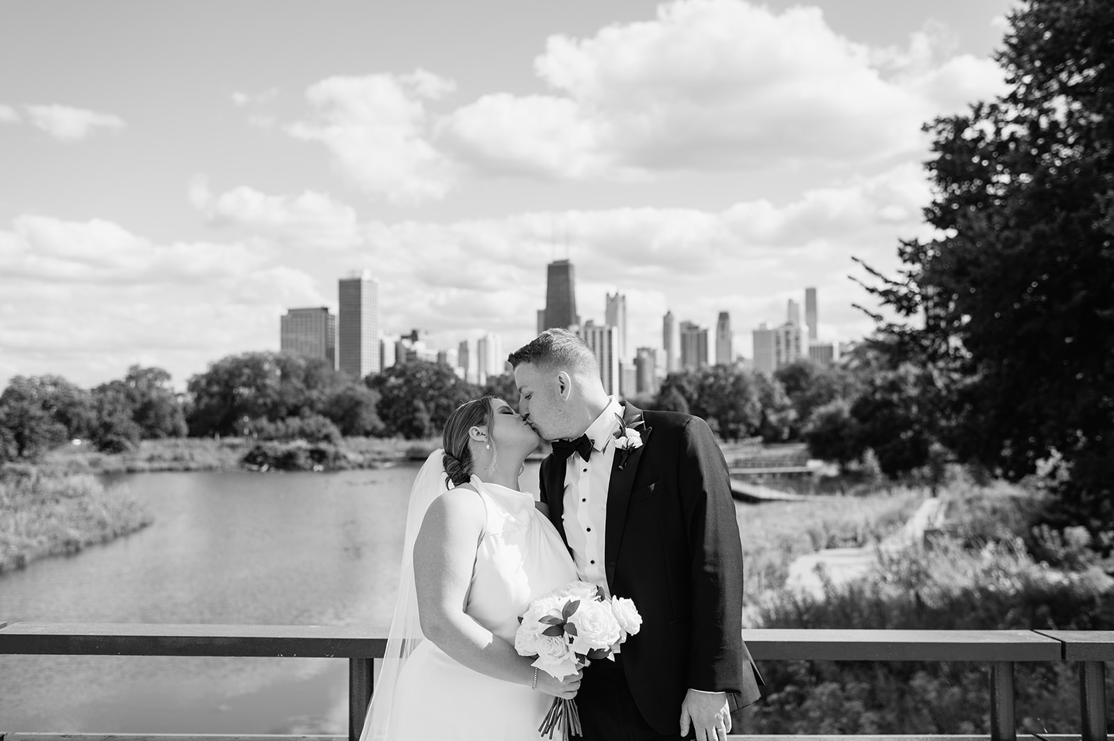 Black and white photo of a bride and groom kissing with the Chicago skyline behind them at Lincoln Park.