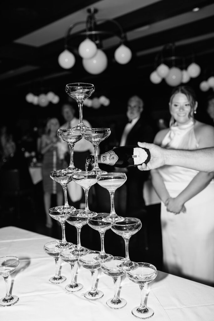 Black and white photo of the bride and groom pouring into their champagne tower.