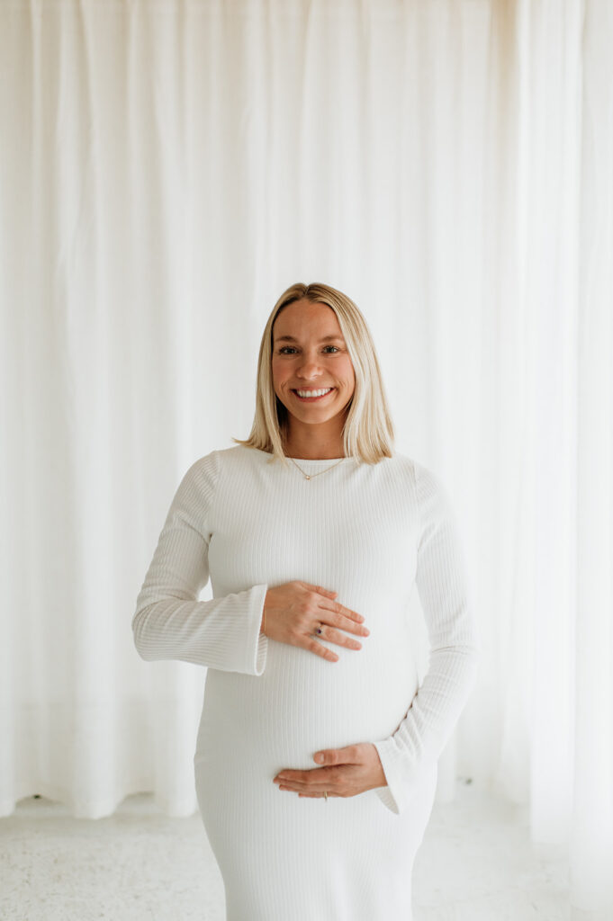 Pregnant woman smiling while resting her hands on her belly during South Bend Indiana maternity photos.