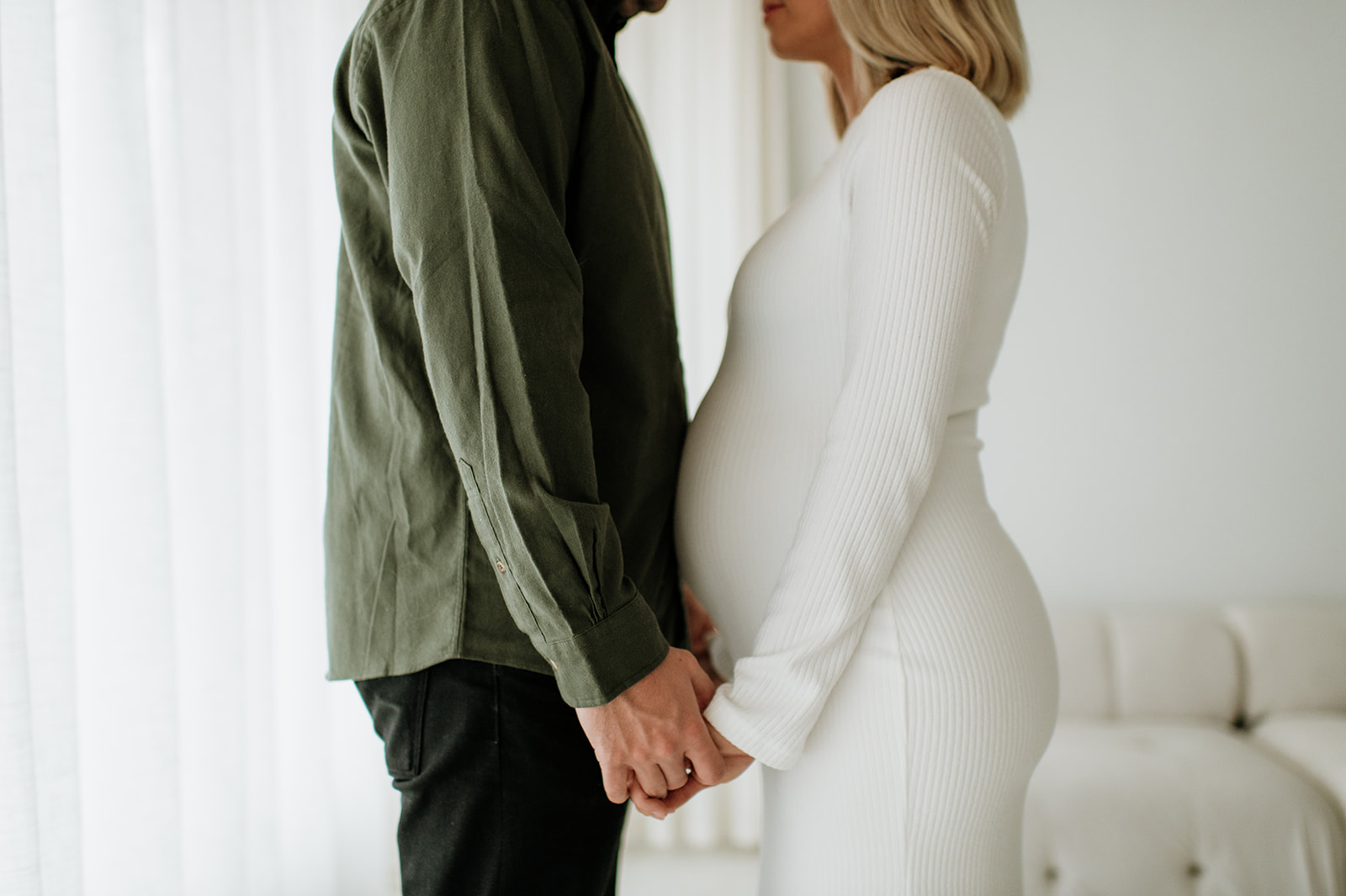 Close-up maternity photo of an expecting couple holding hands with baby bump visible.